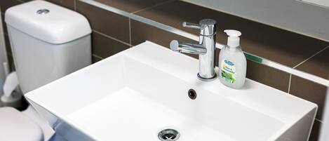 A bathroom with a white sink, a chrome faucet, and a soap dispenser.