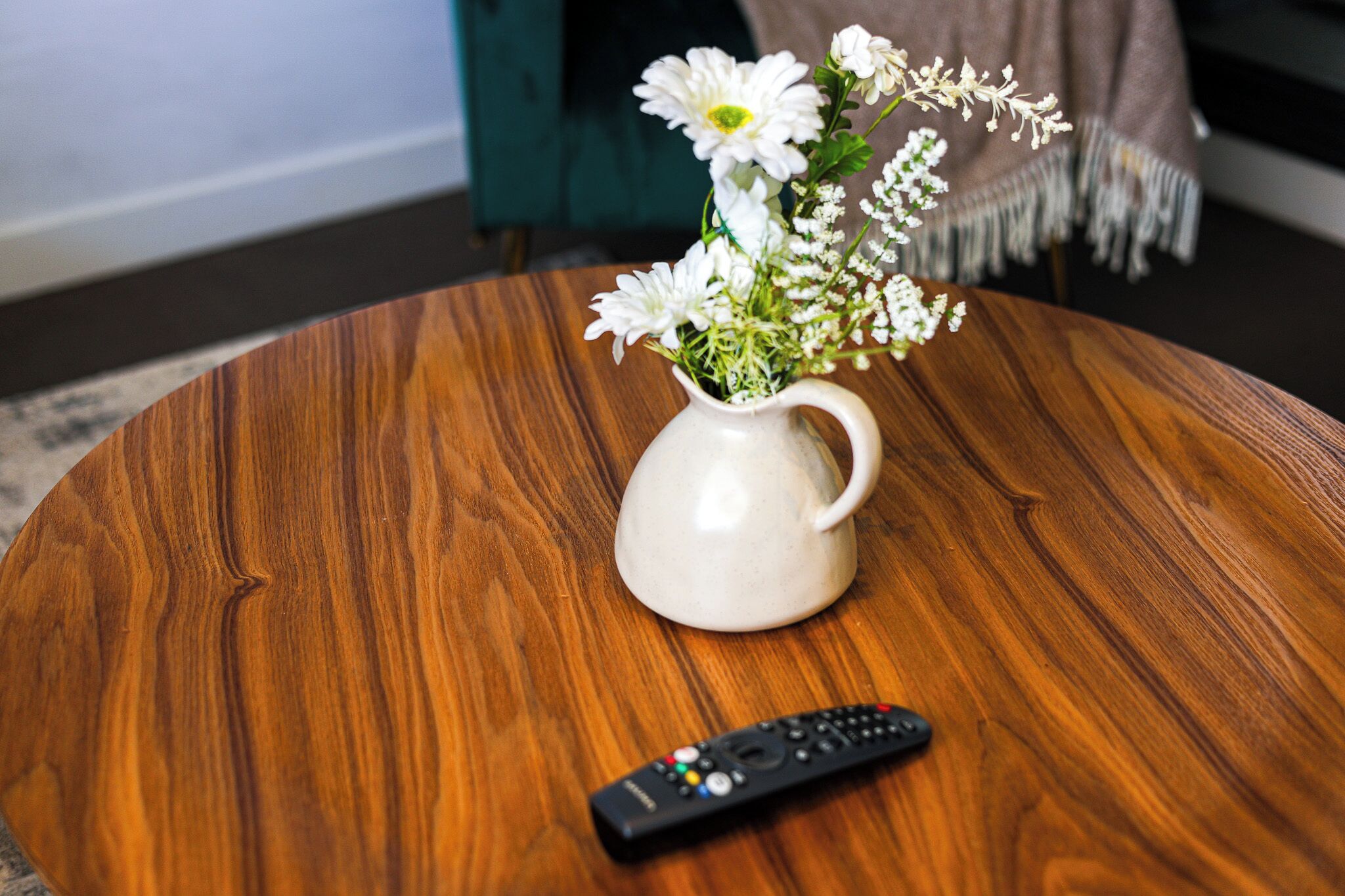 Een witte keramieken karaf met bloemen op een houten tafel.