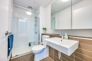 A modern bathroom with a glass-enclosed shower, a white toilet, a large sink, and a mirror above the sink.