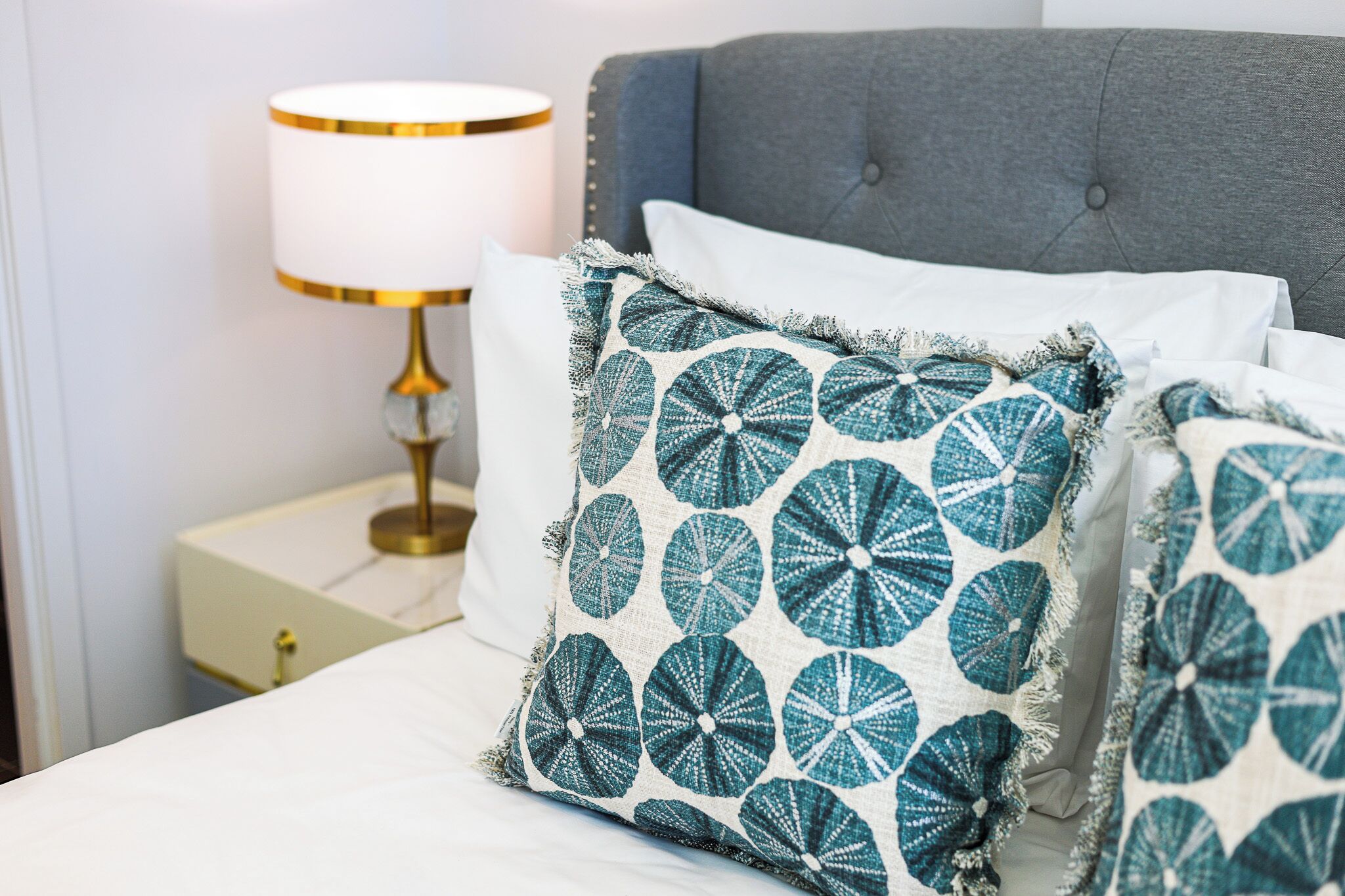 A neatly made bed with a grey headboard, a white pillow, and a decorative pillow with a circular pattern.