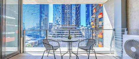 A balcony with a glass door, two chairs, a small round table, and a large air conditioning unit.