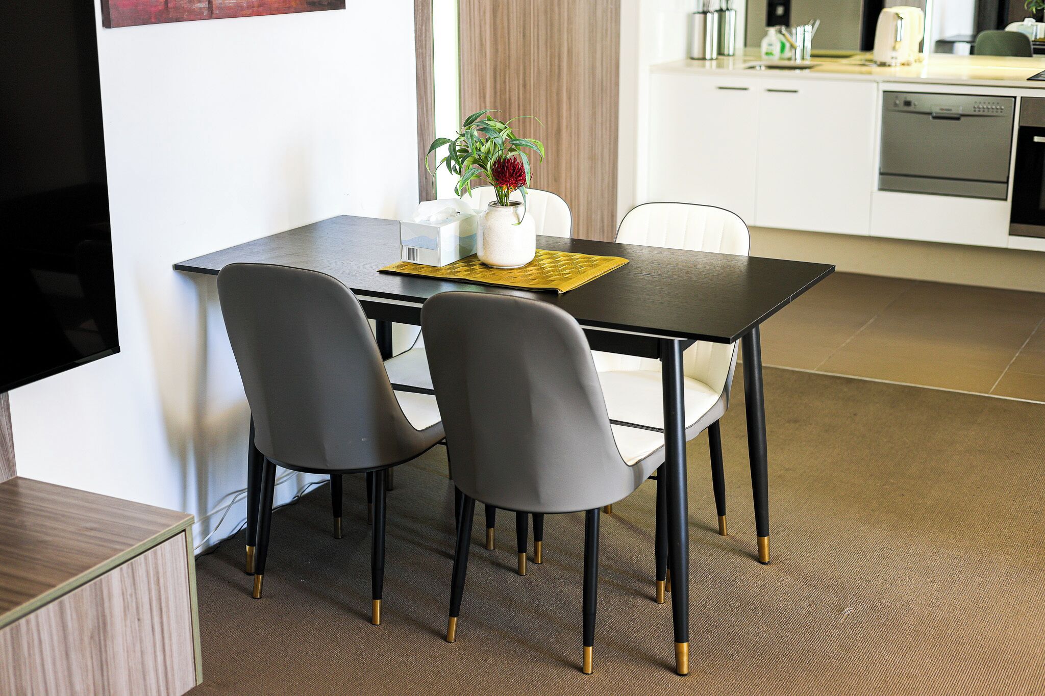 A modern dining area with a dark wooden table, two grey chairs, and a small white vase with a plant.