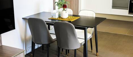 A modern dining area with a dark wooden table, two grey chairs, and a small white vase with a plant.