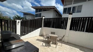 Een terras met een barbecue, een tafel en stoelen.
