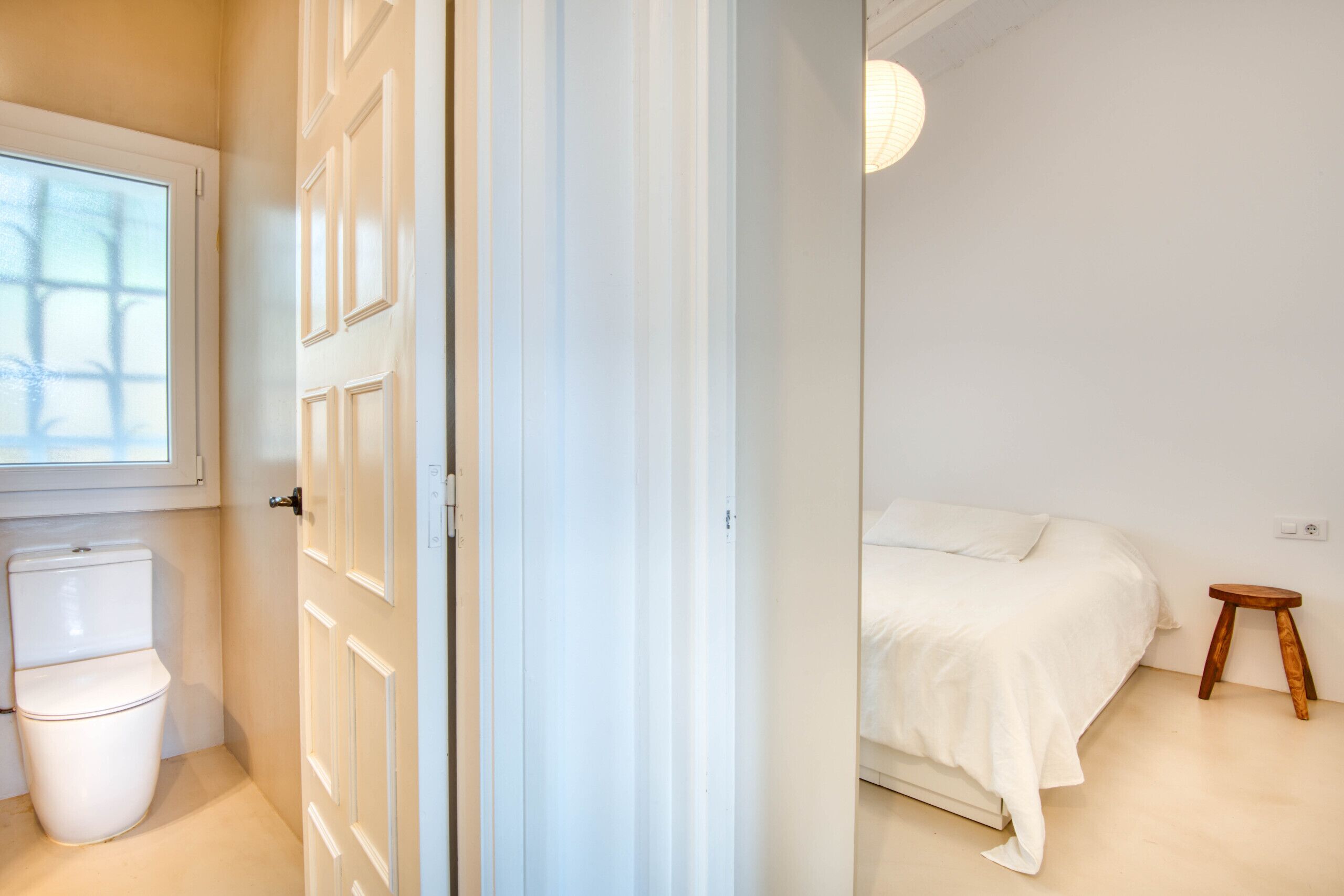 Ein Schlafzimmer mit Bett, einem kleinen Holzhocker, einem Fenster und einer Toilette.
