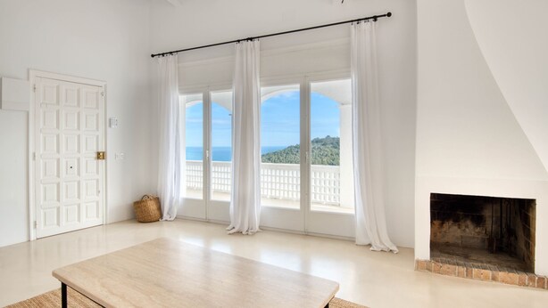 A room with a large window, a fireplace, and a wooden table. - CALMA: Spectacular holiday rental villa with private pool and sea views in Sa Riera, Begur. (Begur)