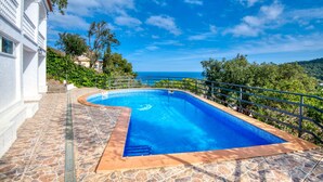 A swimming pool with a stone deck, surrounded by a white building and lush greenery. - CALMA: Spectacular holiday rental villa with private pool and sea views in Sa Riera, Begur. (Begur)
