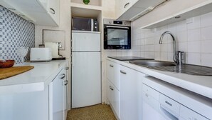 Eine kompakte Küche mit weißen Schränken, einem Geschirrspüler von Bosch, einer Mikrowelle, einem Toaster und einem Spülbecken.
