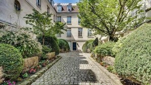 A cobblestone alleyway flanked by neatly trimmed hedges and a row of traditional buildings with multiple windows and a central door. - The Persian Lady Latin Quarter by Mon Petit Faré (Paris)