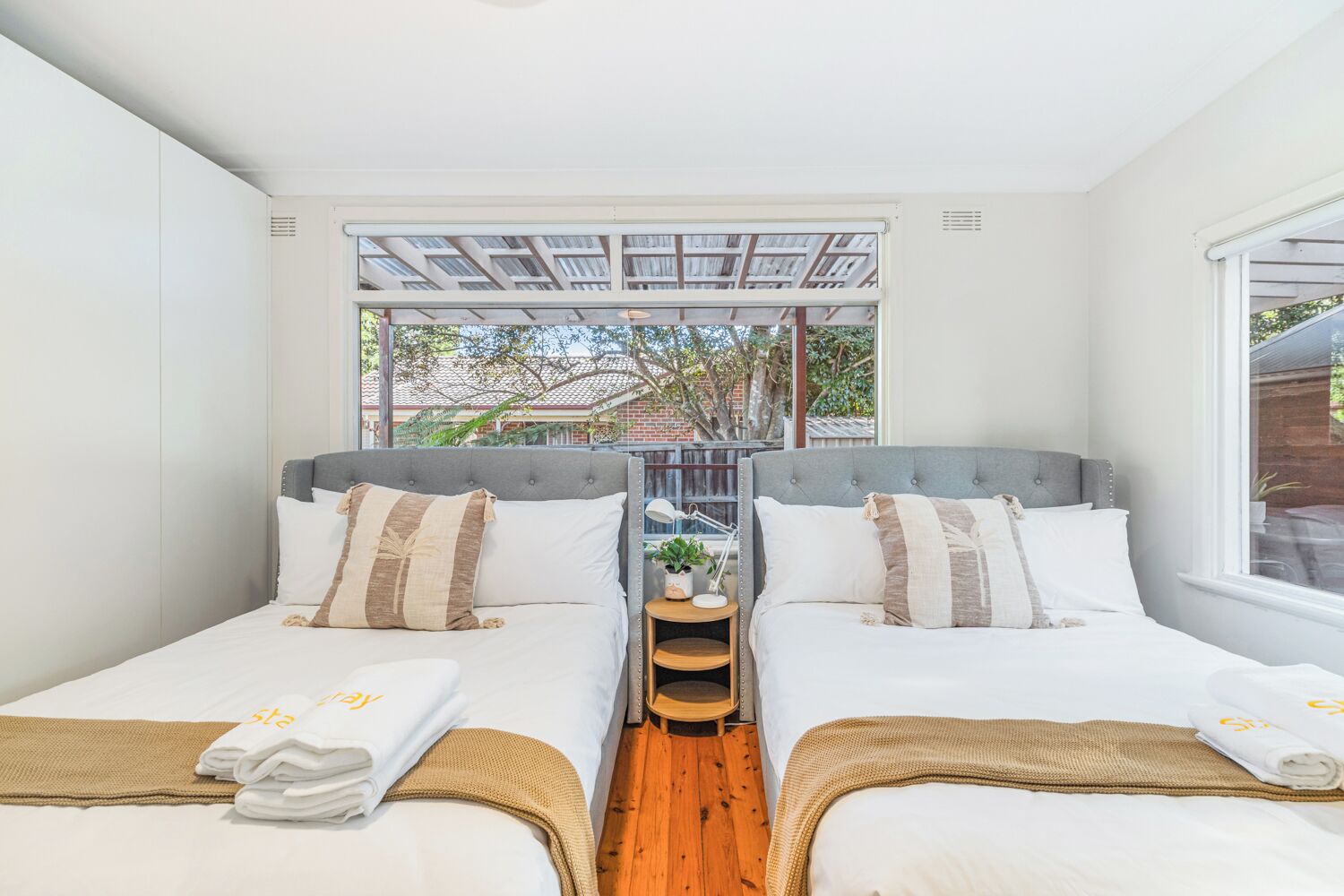 Une chambre double avec deux lits, une petite table et une fenêtre donnant sur un bâtiment en briques et des arbres.