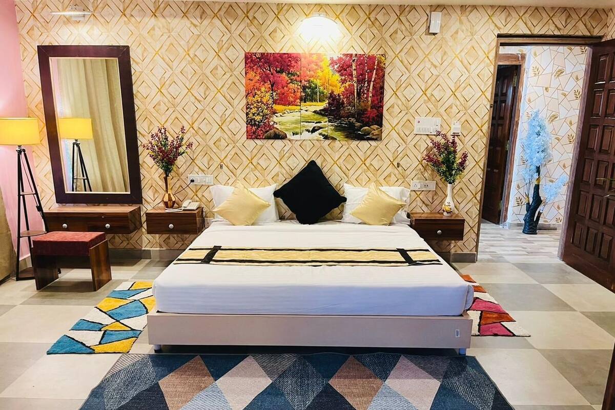 Une chambre d’hôtel avec un lit, des tables de chevet, un miroir, un tableau et un tapis à motifs.