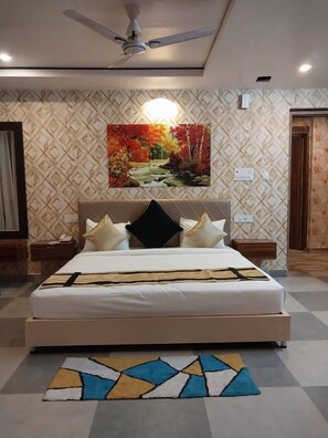A bedroom with a bed, nightstands, a ceiling fan, a wall-mounted painting, and a patterned rug. - Gulmohar guest house (Balasore)