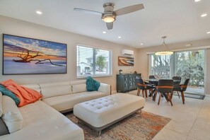 A modern living room with a sectional sofa, a dining area with a table and chairs, and a ceiling fan.