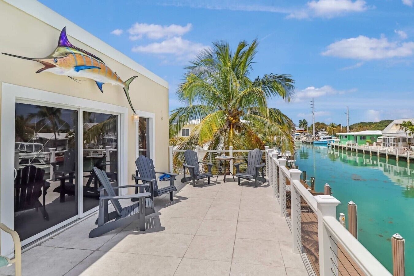 Eine Resort-Terrasse mit Sitzgelegenheiten im Freien, Blick auf eine Marina und einem Wandgemälde mit Segelfischen.