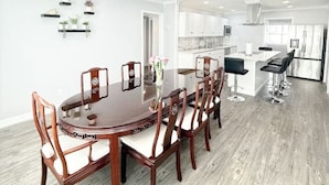 Una cocina moderna con armarios blancos, una isla central con taburetes altos y un comedor con mesa y sillas de madera.