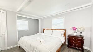 Un dormitorio con una cama, un aparador y dos ventanas.