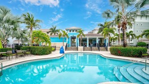 Ein Poolbereich eines Resorts mit klarem, blauem Pool, Palmen und einem Gebäude mit blauen und weißen Außenwänden.