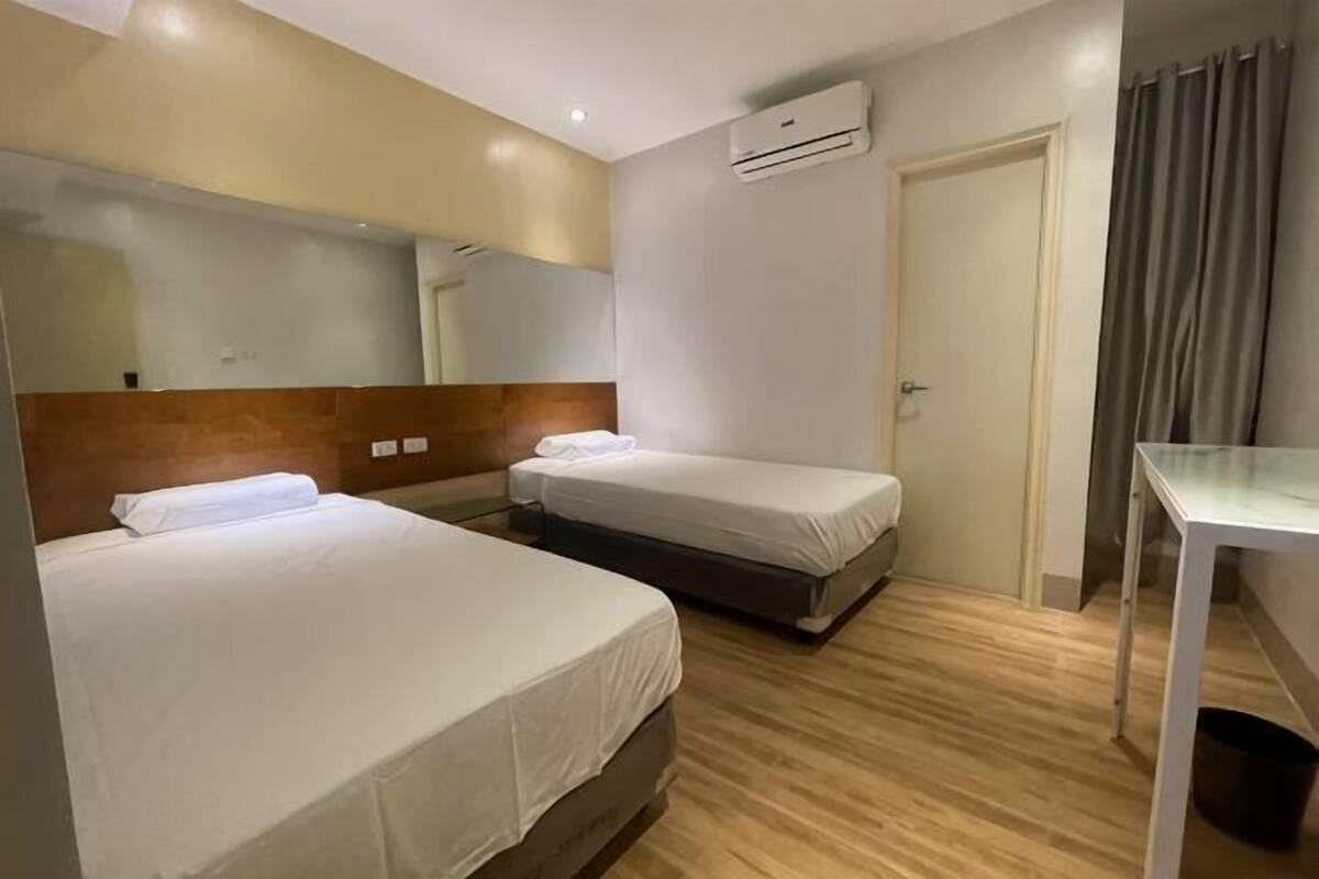 A hotel room with two beds, a desk, a mirror, a door, and an air conditioning unit.