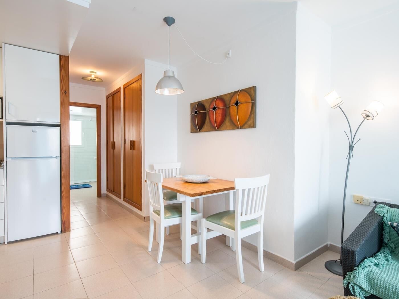 Una cocina compacta con una mesa de comedor, sillas, un refrigerador y una lámpara de pie.