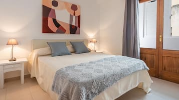 Un dormitorio con cama, dos mesitas de noche, una mesita auxiliar, un cuadro en la pared y una puerta de madera.