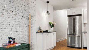 A modern kitchen with white cabinets, a stainless steel refrigerator, and a wooden floor. - ★HostWise Stays★ Stylish War Streets Retreat | Easy Walk to Stadiums & Dining (Pittsburgh)
