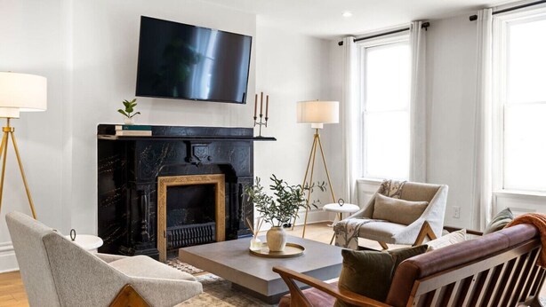 A modern living room with a fireplace, a flat-screen TV, and two armchairs. - ★HostWise Stays★ Stylish War Streets Retreat | Easy Walk to Stadiums & Dining (Pittsburgh)