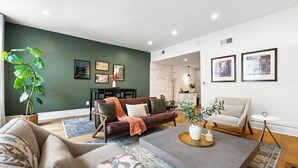 A modern living room with a dark green accent wall, a brown leather sofa, a grey sectional, and a coffee table with decorative items. - ★HostWise Stays★ Stylish War Streets Retreat | Easy Walk to Stadiums & Dining (Pittsburgh)