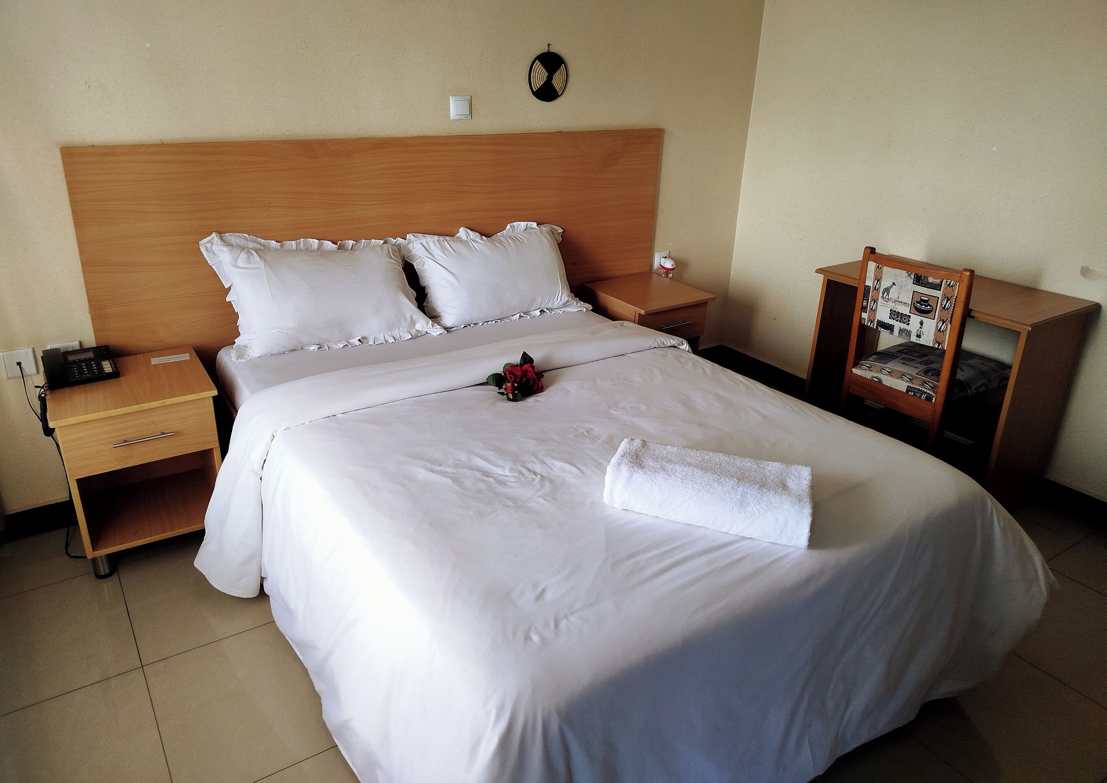 A neatly made bed with white linens, a bedside table with a phone, and a small nightstand with a lamp.