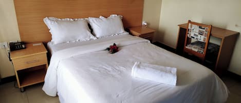 Un lit bien fait, avec du linge de lit blanc, une table de chevet avec un téléphone et une petite table de nuit avec une lampe.