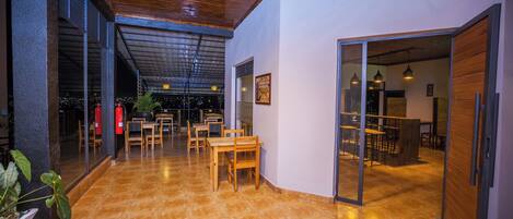 A spacious indoor area with hexagonal tiled flooring, wooden tables and chairs, and a glass door leading to another room.