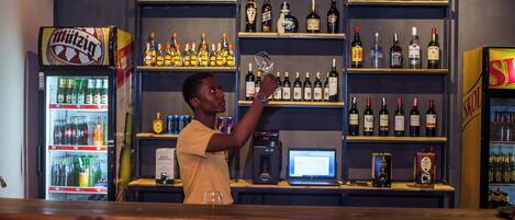 A bar with shelves of liquor bottles, a refrigerator with drinks, and a computer on the counter.