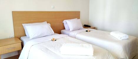 Ein Hotelzimmer mit zwei Betten, weißen Bettwäsche, einem hölzernen Kopfteil, einem Nachttisch, einem Telefon und Wandbildern.