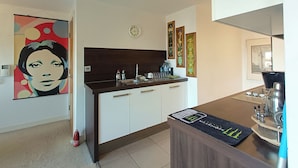 A modern kitchen with a dark countertop, white cabinets, and a coffee machine. There is a clock on the wall and a framed artwork above the cabinets. - 1 Bed Flat - Sleeps 5 - Pets - Garden - Parking (Manchester)