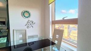 A modern office space with a glass table, two chairs, a decorative wall piece, and a window with a city view. - 1 Bed Flat - Sleeps 5 - Pets - Garden - Parking (Manchester)