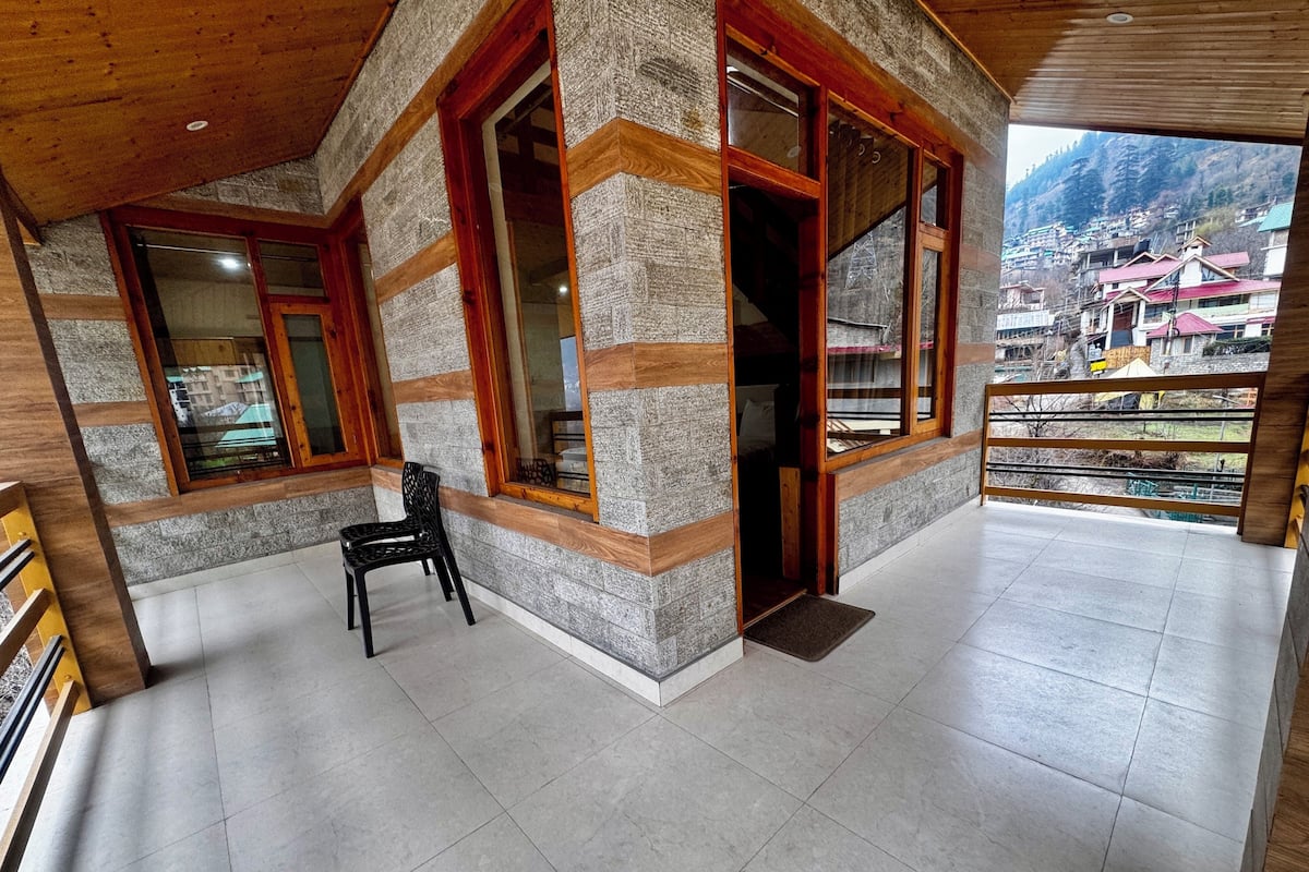 A spacious balcony with a view of a mountainous village, stone walls, and wooden beams.