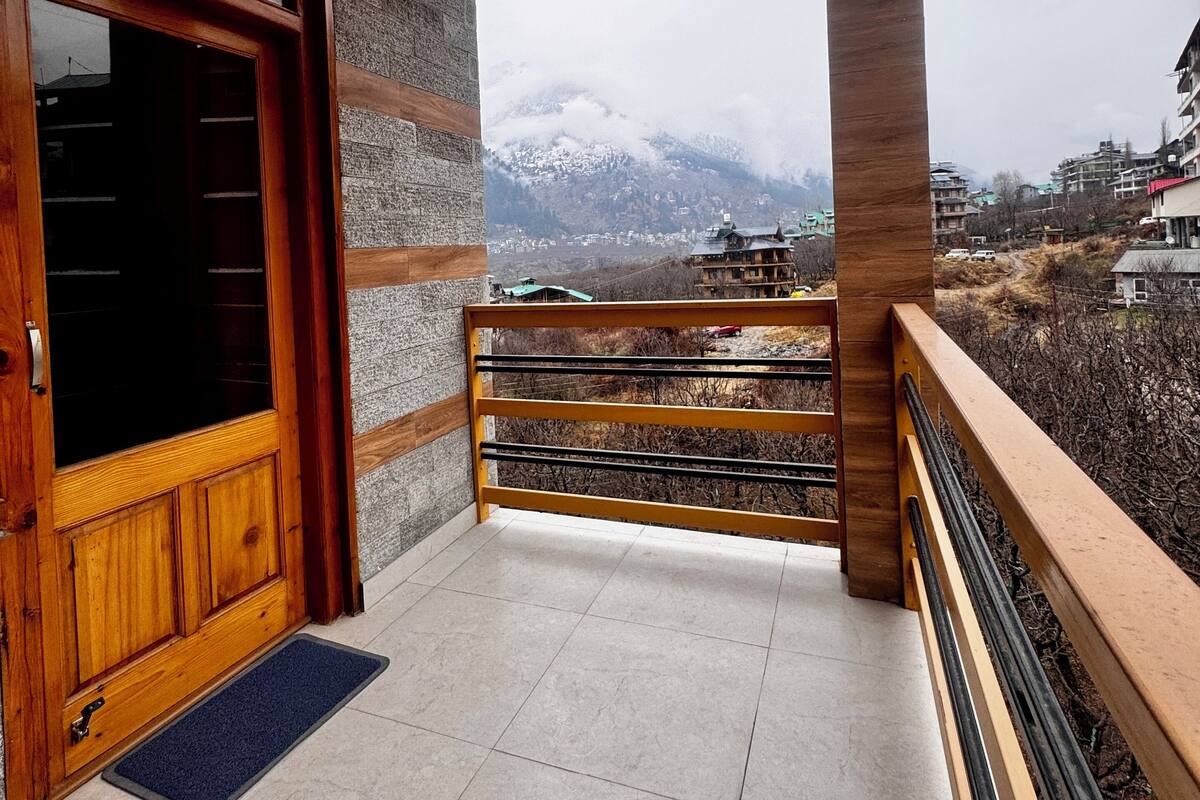 A balcony with a view of snow-capped mountains, a wooden door, and a tiled floor.