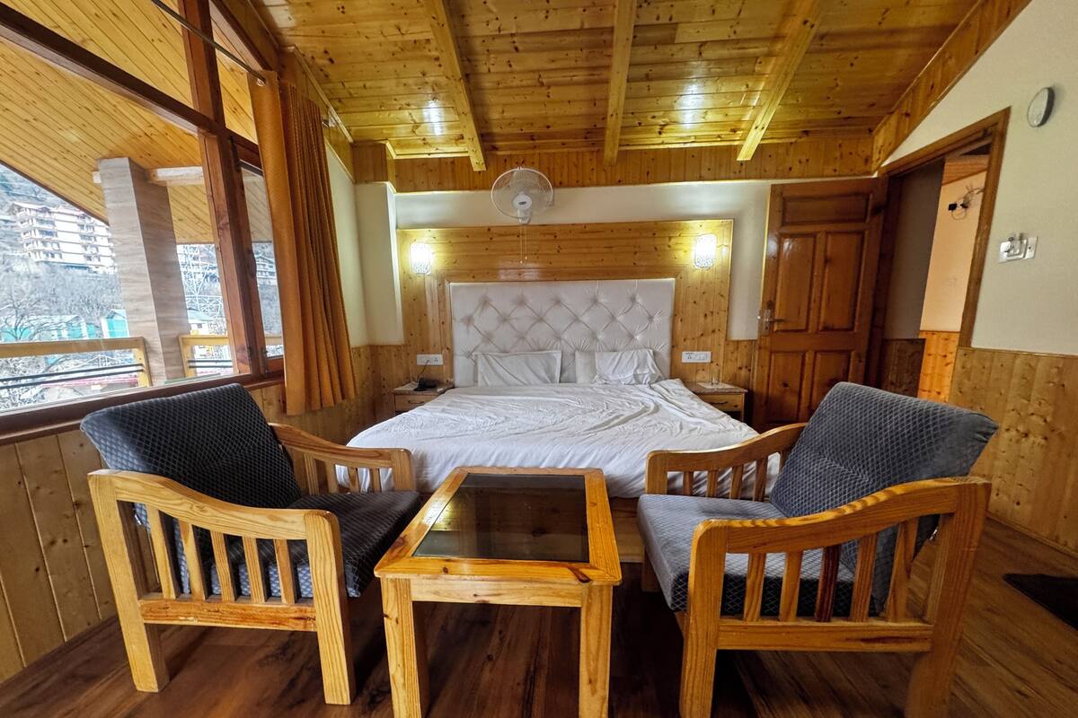 A wooden-floored room with a bed, two chairs, a table, and a ceiling fan.