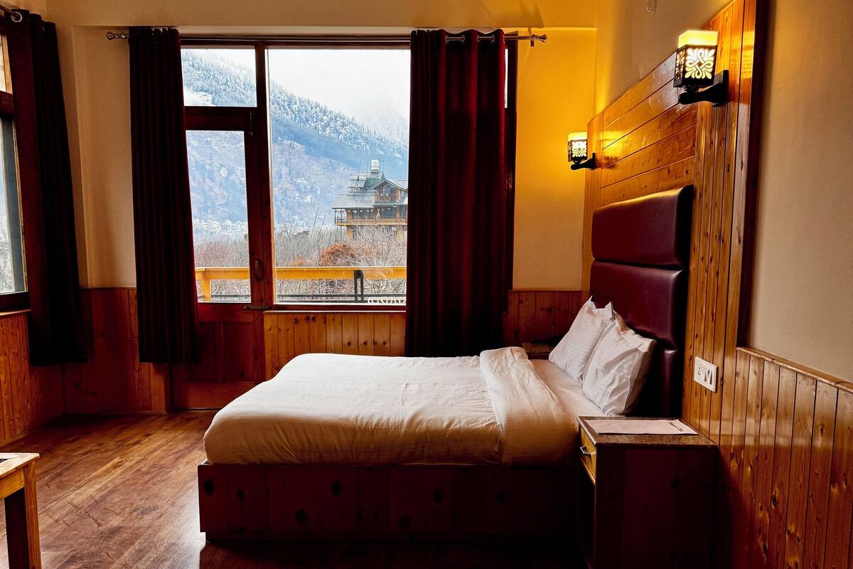 A wooden-paneled bedroom with a large bed, a nightstand, a ceiling fan, and a window offering a mountain view.