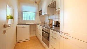 Eine Küche mit weißen Schränken, einem Geschirrspüler, einem Backofen und einem Fenster mit Jalousien.