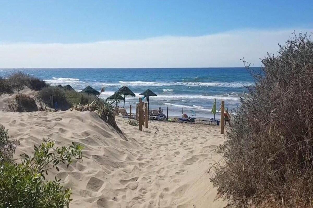 A sandy beach with umbrellas and lounge chairs, leading to the ocean.