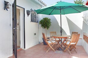 A patio with a table and chairs, a green umbrella, a potted plant, and a wall-mounted light fixture. - Cosy Holiday Home Near Beach (Marbella)
