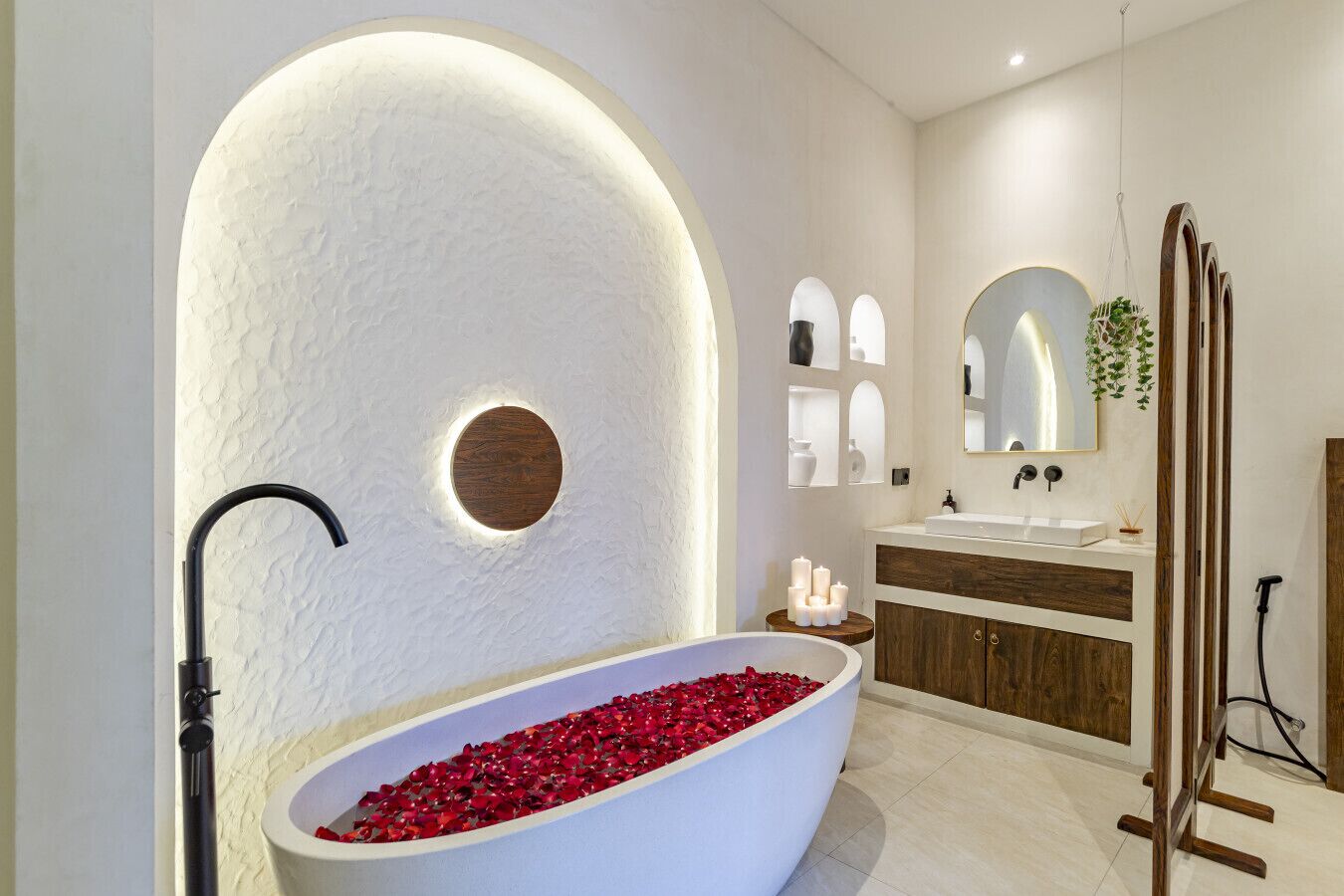 Une salle de bain moderne avec une baignoire sur pieds remplie de pétales de roses, un meuble-lavabo en bois et un grand miroir au-dessus du lavabo.