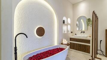 Une salle de bain moderne avec une baignoire sur pieds remplie de pétales de roses, un meuble-lavabo en bois et un grand miroir au-dessus du lavabo.