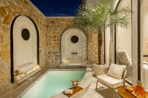 Ein Wellnessbereich mit Steinwand, Pool, Liegestuhl und Topfpflanze.