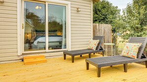 Une terrasse avec deux chaises longues et une petite table, une porte-fenêtre coulissante et une clôture en bois.