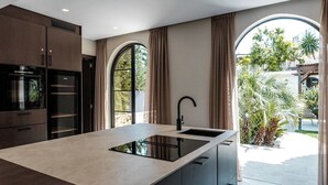 Una cocina moderna con una isla central, electrodomésticos integrados y vistas al jardín exterior.