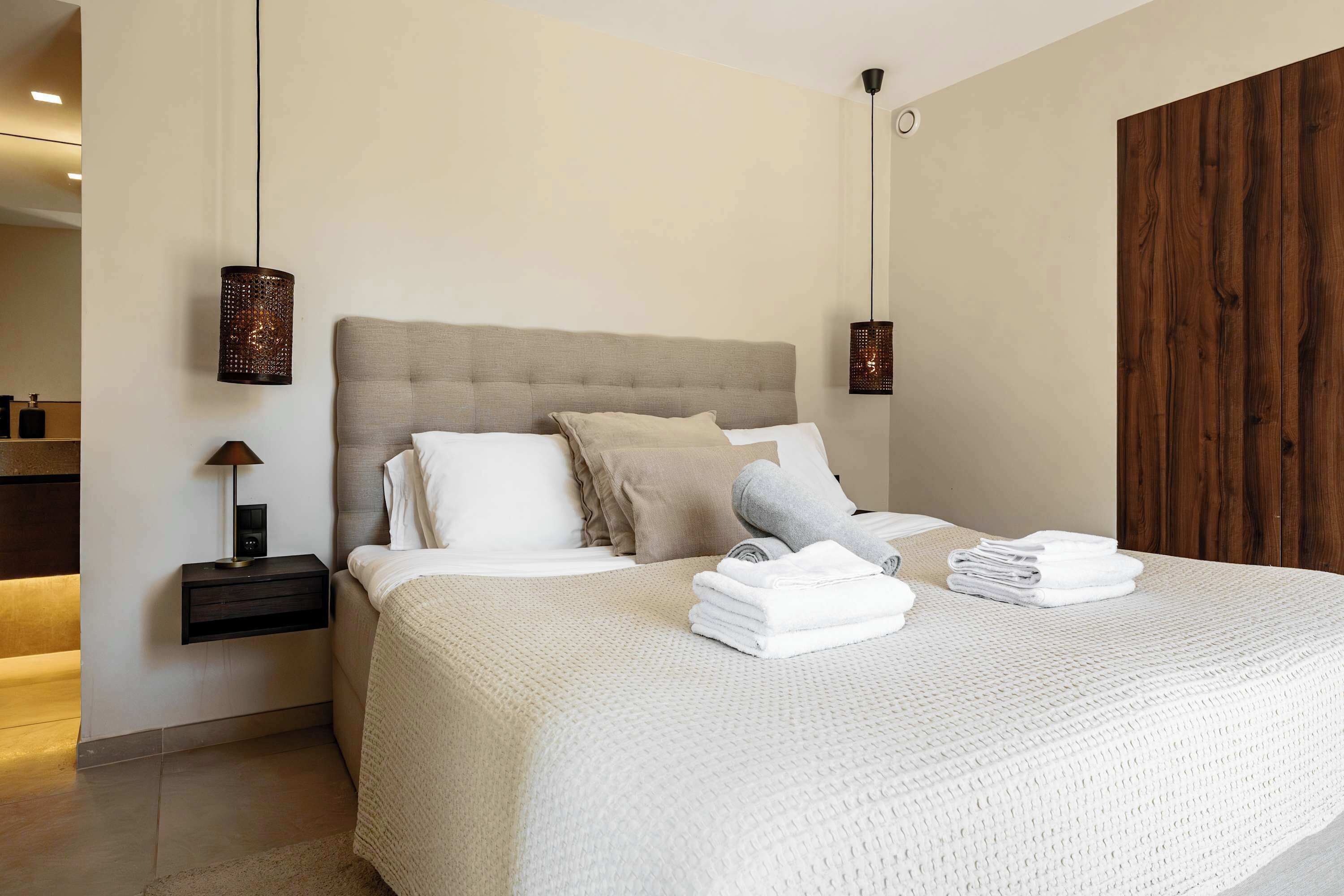 A modern bedroom with a large bed, two bedside lamps, a nightstand, and a wooden panel wall.