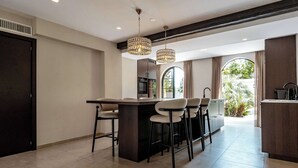 Cocina moderna con una isla central, taburetes de bar, iluminación colgante y vistas al exterior.
