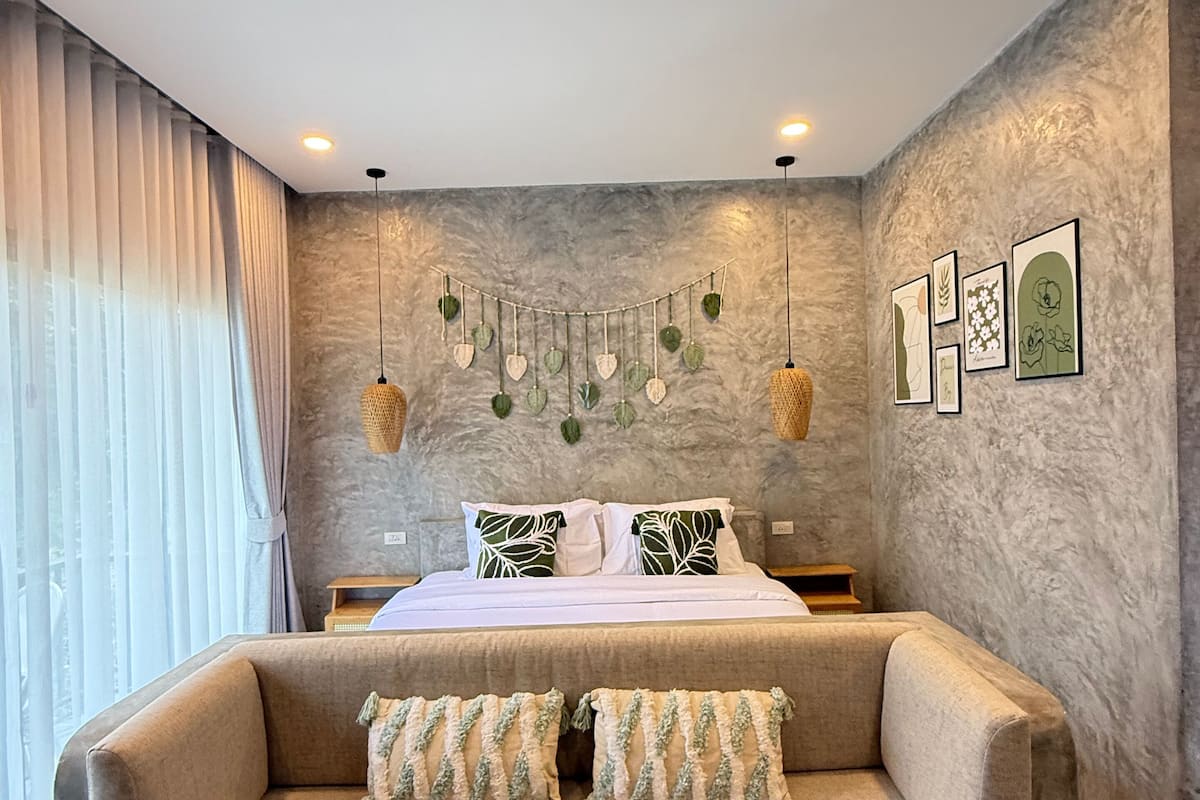 A bedroom with a bed, a sofa, a hanging plant, and framed artwork on the wall.