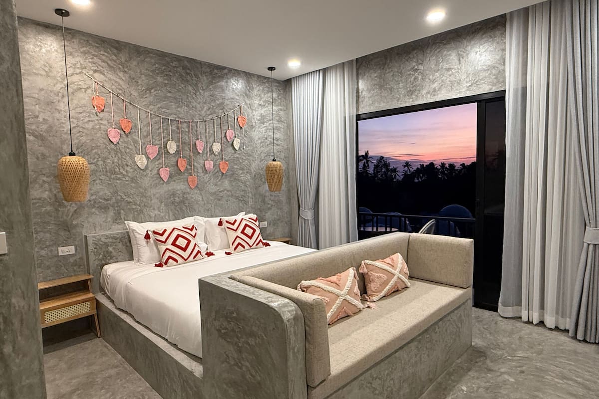 A modern bedroom with a bed, a sofa, a decorative wall, and a large window with curtains.